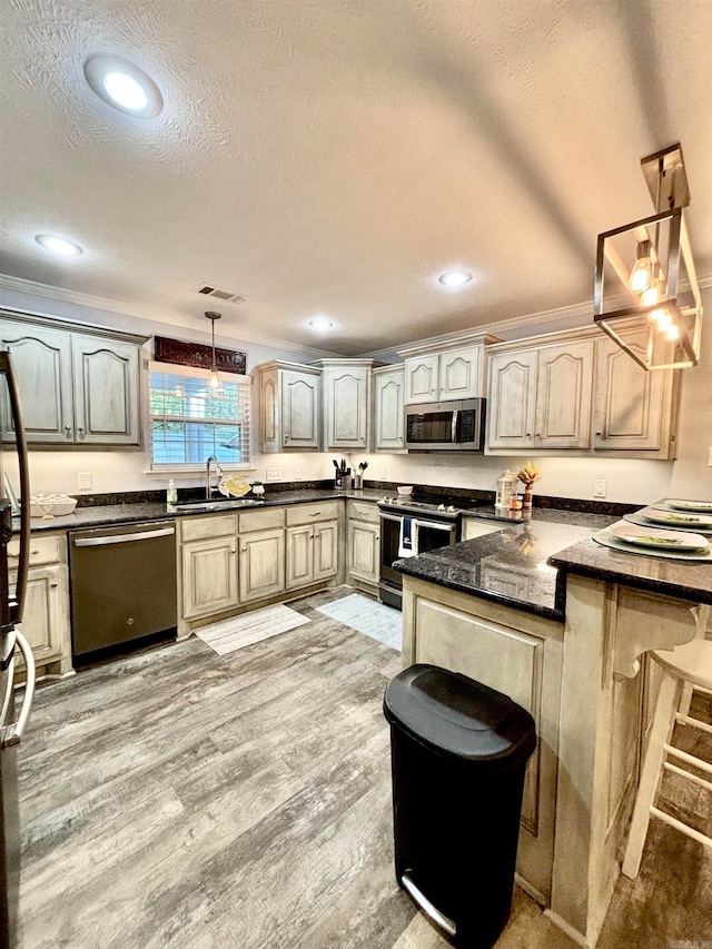 kitchen with hanging light fixtures, sink, a textured ceiling, light hardwood / wood-style flooring, and appliances with stainless steel finishes