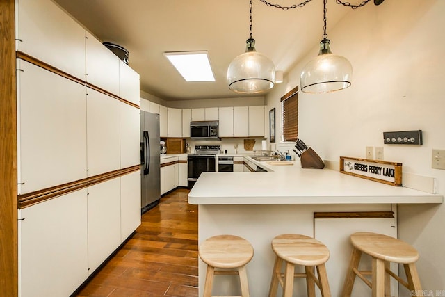 kitchen featuring stainless steel appliances, white cabinetry, a kitchen bar, and dark hardwood / wood-style floors