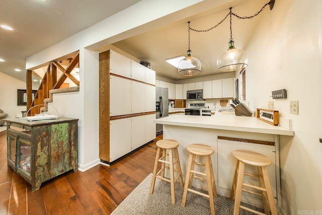 kitchen with dark hardwood / wood-style floors, white cabinets, kitchen peninsula, appliances with stainless steel finishes, and decorative light fixtures