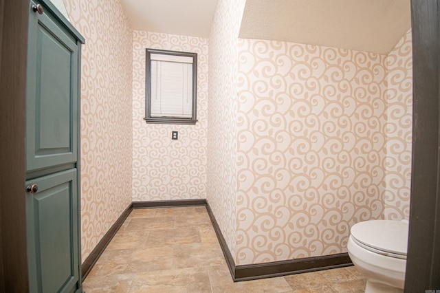 bathroom with stone finish floor, baseboards, wallpapered walls, and toilet