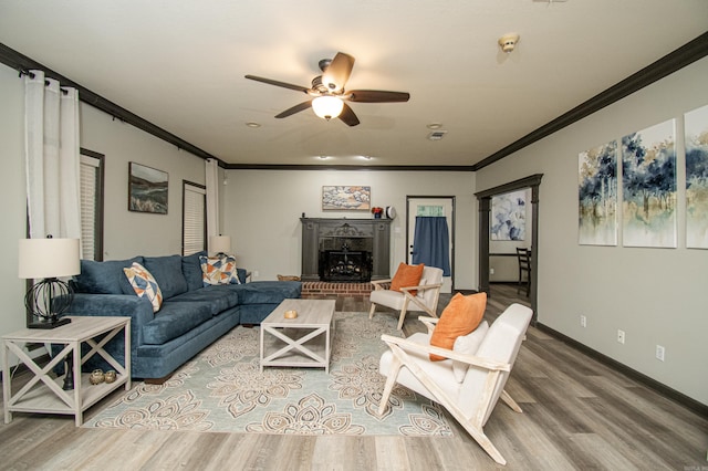 living area with ornamental molding, baseboards, a ceiling fan, a fireplace, and wood finished floors