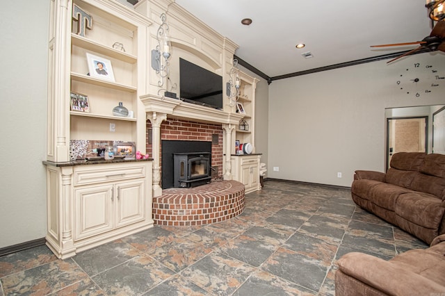 living area with a wood stove, ornamental molding, stone finish floor, baseboards, and a ceiling fan