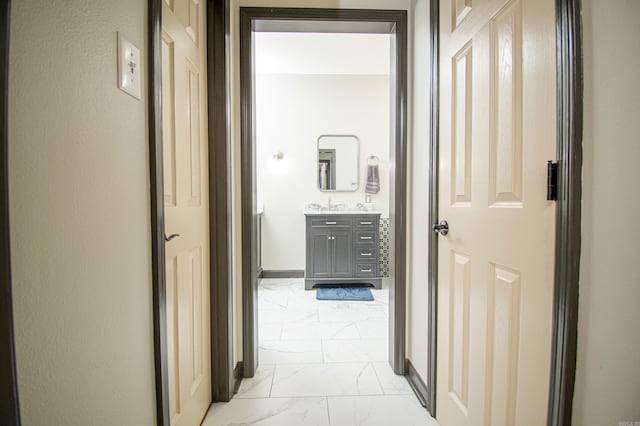hallway with marble finish floor, a sink, and baseboards