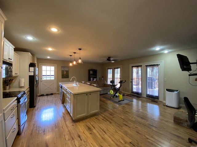 kitchen featuring stainless steel fridge, light hardwood / wood-style floors, white cabinets, white gas stove, and a center island with sink