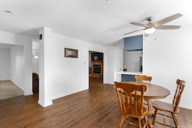 dining room with dark hardwood / wood-style flooring, ceiling fan, and a brick fireplace