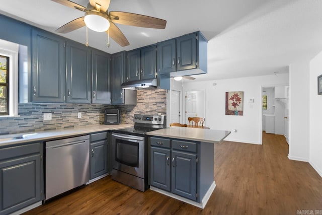 kitchen with stainless steel appliances, kitchen peninsula, dark wood-type flooring, and tasteful backsplash