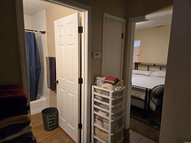 bathroom with a textured ceiling, wood-type flooring, and shower / bathtub combination with curtain