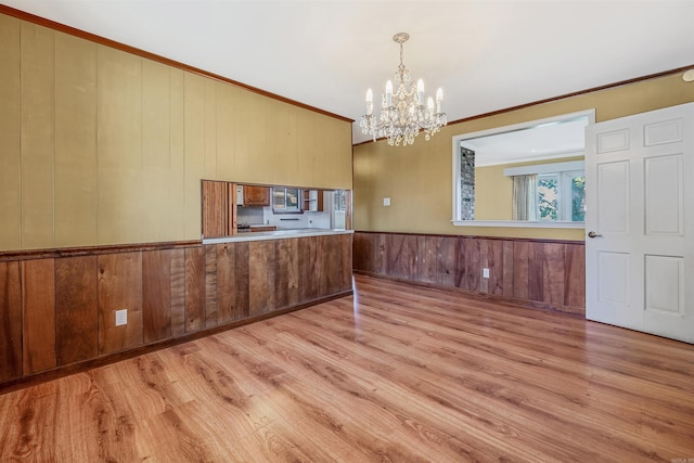 interior space featuring a notable chandelier, wooden walls, crown molding, and light hardwood / wood-style floors