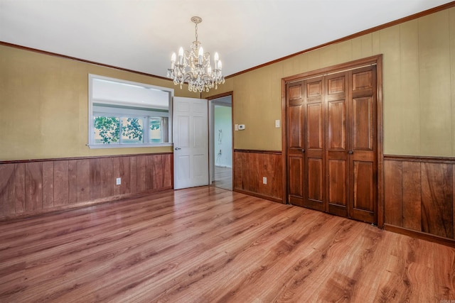 unfurnished bedroom with ornamental molding, wooden walls, a closet, an inviting chandelier, and light wood-type flooring