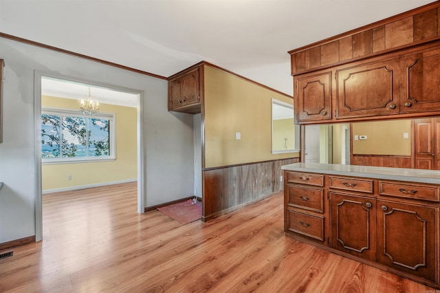 kitchen featuring light wood-type flooring, a chandelier, wood walls, decorative light fixtures, and crown molding