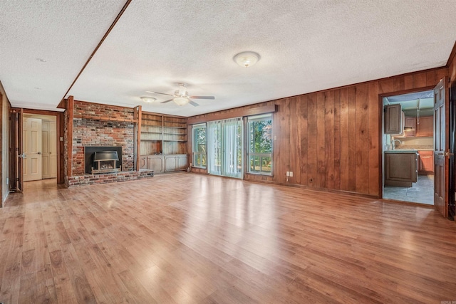 unfurnished living room featuring ceiling fan, a wood stove, a textured ceiling, light hardwood / wood-style flooring, and wooden walls