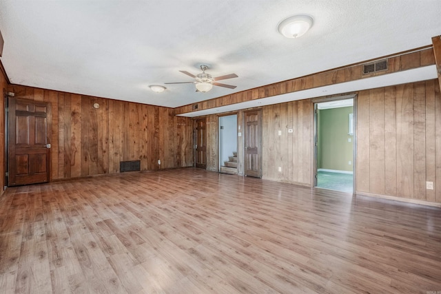 unfurnished living room featuring ceiling fan, wooden walls, light wood-type flooring, and a textured ceiling