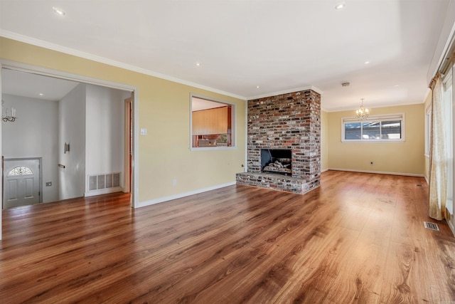 unfurnished living room featuring a brick fireplace, a chandelier, hardwood / wood-style floors, and crown molding