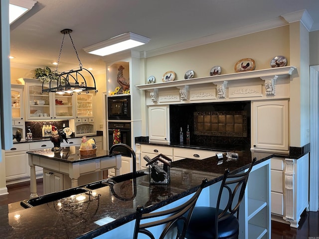 kitchen featuring pendant lighting, white cabinets, a kitchen island, black appliances, and a kitchen bar