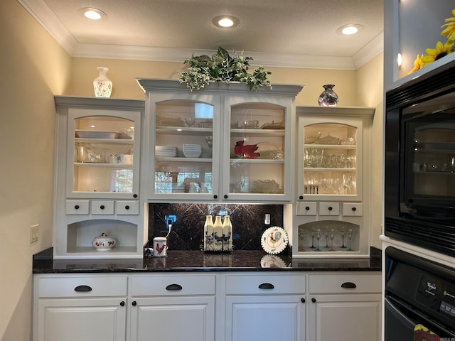 bar featuring tasteful backsplash, black appliances, white cabinetry, dark stone counters, and crown molding