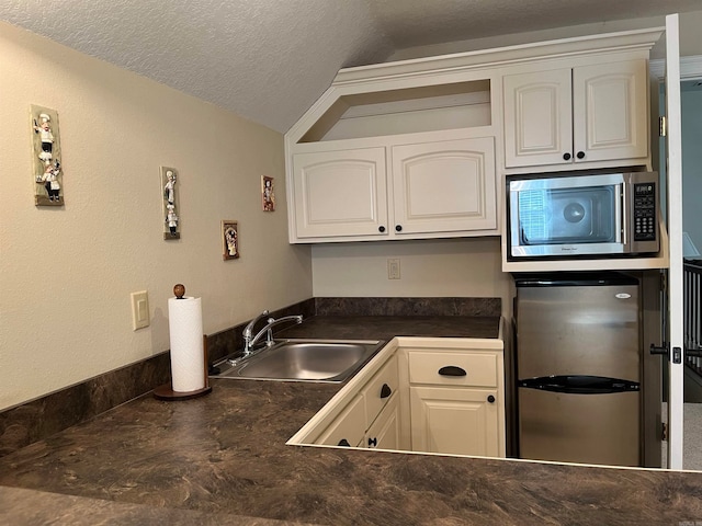 kitchen with a textured ceiling, sink, white cabinets, vaulted ceiling, and appliances with stainless steel finishes