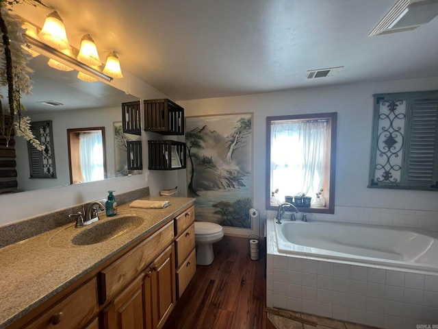 bathroom with wood-type flooring, tiled tub, vanity, and toilet