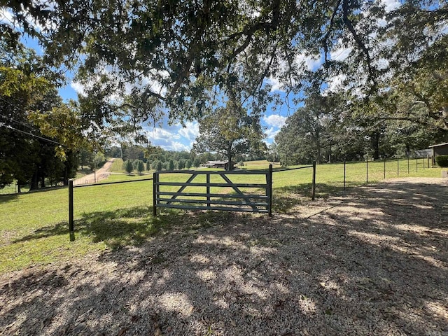 view of gate with a lawn and a rural view