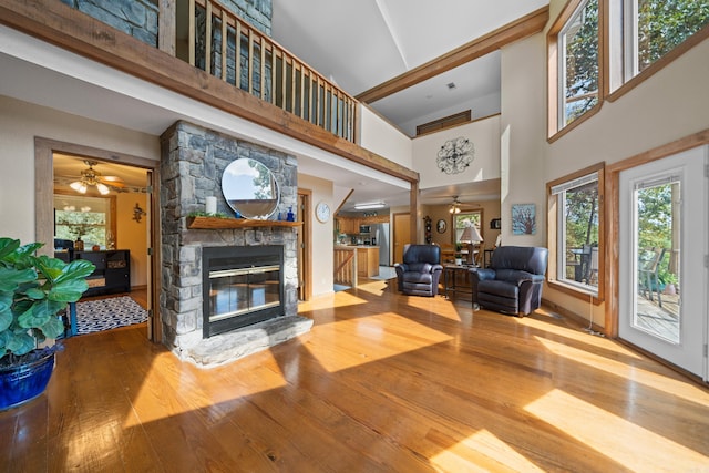 living room featuring ceiling fan, a fireplace, a towering ceiling, and hardwood / wood-style floors