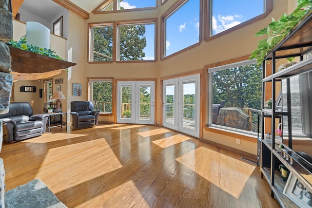 living room with high vaulted ceiling, hardwood / wood-style floors, a healthy amount of sunlight, and french doors