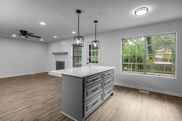 kitchen featuring a brick fireplace, pendant lighting, a center island, ceiling fan, and hardwood / wood-style flooring