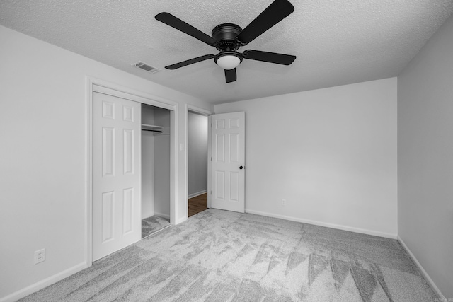 unfurnished bedroom featuring a textured ceiling, ceiling fan, light colored carpet, and a closet