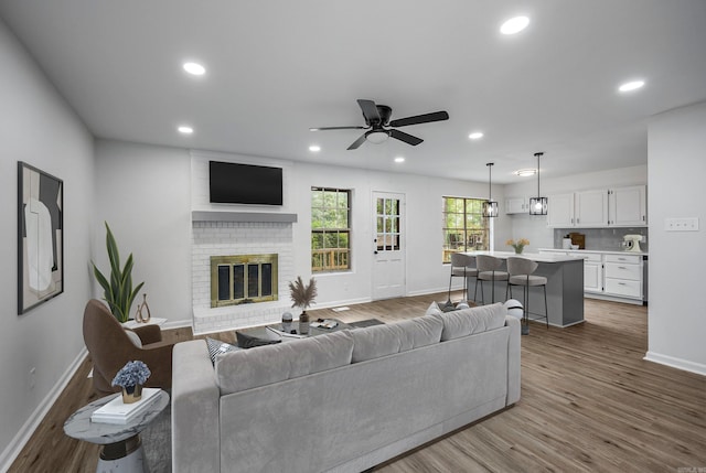 living room with hardwood / wood-style floors, ceiling fan, and a brick fireplace