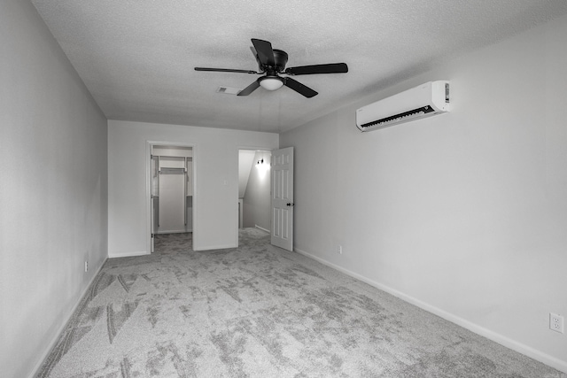 unfurnished bedroom with a closet, ceiling fan, a walk in closet, a wall unit AC, and light colored carpet