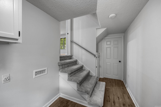 staircase featuring a textured ceiling and hardwood / wood-style floors