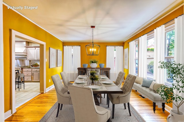 dining space with ornamental molding, light wood-type flooring, and a notable chandelier