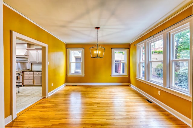 unfurnished dining area featuring an inviting chandelier, light wood-type flooring, plenty of natural light, and ornamental molding