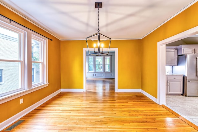 unfurnished dining area with light wood-type flooring, crown molding, and a chandelier