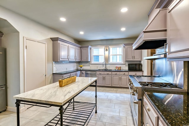 kitchen featuring dark stone counters, custom exhaust hood, gray cabinetry, stainless steel appliances, and light tile patterned floors