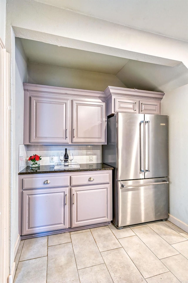 kitchen featuring lofted ceiling, dark stone countertops, backsplash, and stainless steel refrigerator