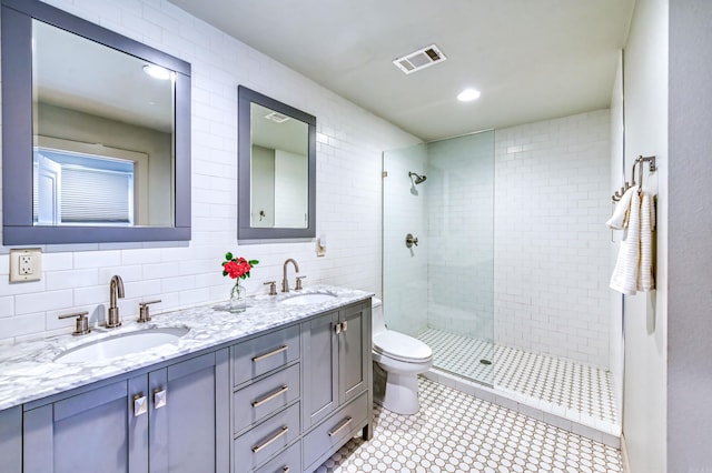 bathroom featuring a tile shower, vanity, tile walls, and toilet