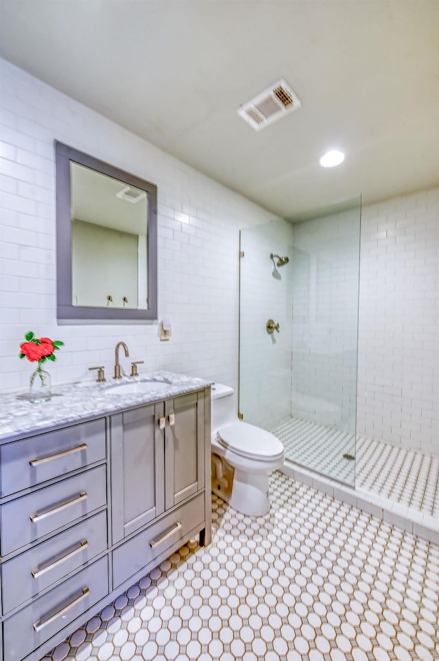 bathroom with tile walls, tile patterned flooring, a shower with shower door, vanity, and toilet