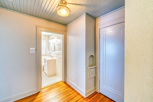 corridor featuring light hardwood / wood-style flooring, crown molding, sink, and wooden ceiling