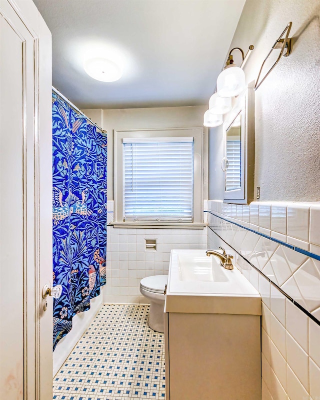 bathroom with tile walls, a shower with curtain, vanity, toilet, and tile patterned floors