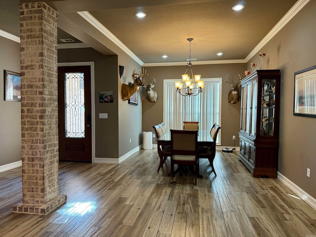 dining space with a textured ceiling, wood-type flooring, crown molding, an inviting chandelier, and decorative columns