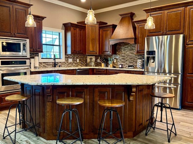 kitchen with appliances with stainless steel finishes, a kitchen island, pendant lighting, a kitchen bar, and custom exhaust hood