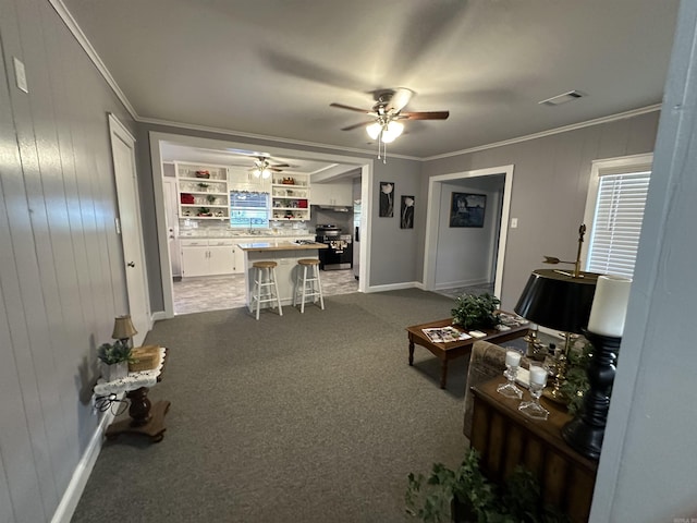 living area with crown molding, dark colored carpet, ceiling fan, visible vents, and baseboards