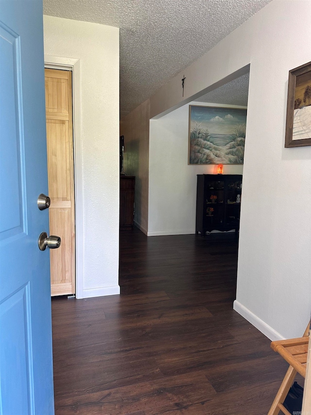 hall with a textured ceiling and dark hardwood / wood-style flooring