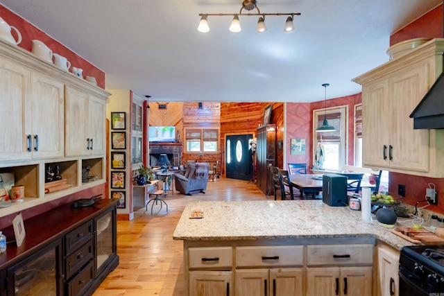 kitchen with light stone counters, pendant lighting, light hardwood / wood-style flooring, wooden walls, and black range