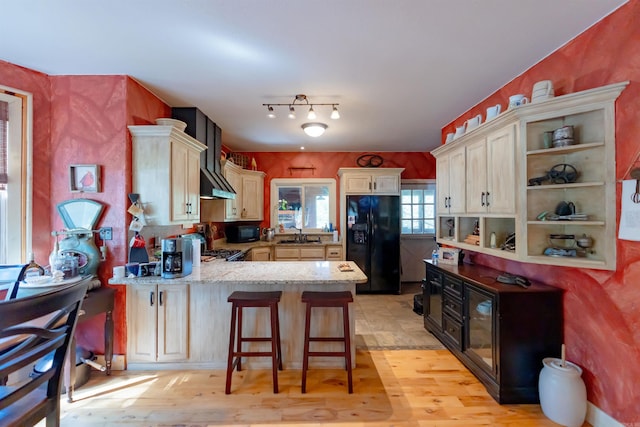 kitchen with light wood-type flooring, black appliances, kitchen peninsula, and a breakfast bar area