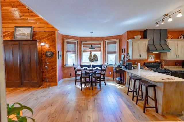 kitchen featuring black range with gas stovetop, wood walls, light stone countertops, light hardwood / wood-style flooring, and premium range hood