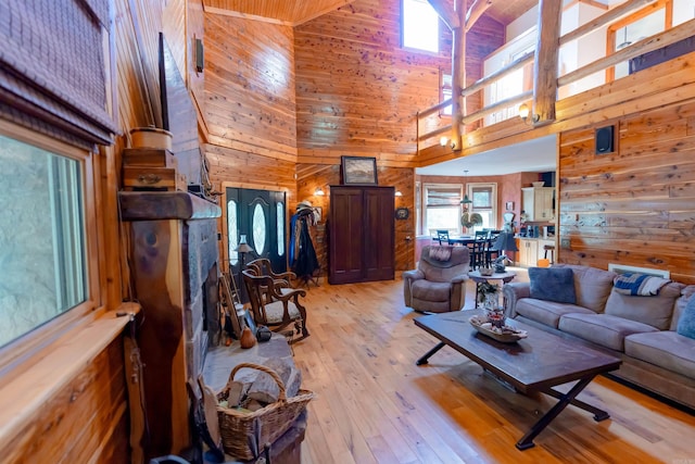 living room with high vaulted ceiling, wood walls, and light hardwood / wood-style flooring