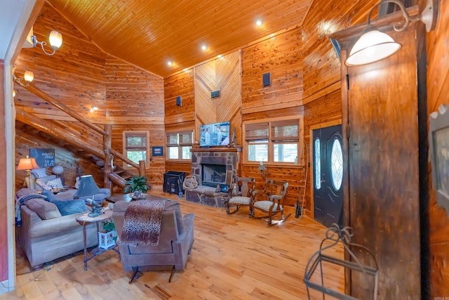 living room featuring wood ceiling, light wood-type flooring, high vaulted ceiling, wooden walls, and a stone fireplace