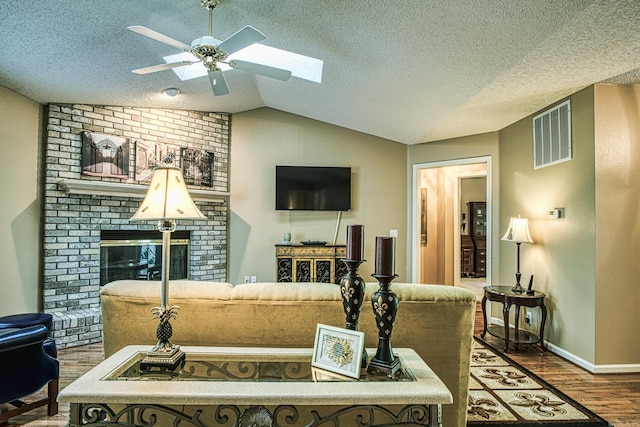 living room with a brick fireplace, a textured ceiling, vaulted ceiling with skylight, ceiling fan, and hardwood / wood-style floors