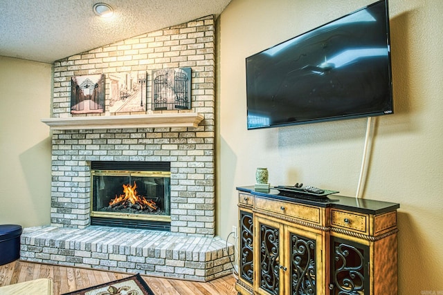 living room with a textured ceiling, a fireplace, hardwood / wood-style floors, and vaulted ceiling