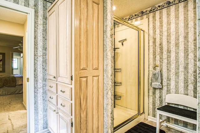 bathroom featuring ceiling fan, a shower with shower door, and a textured ceiling